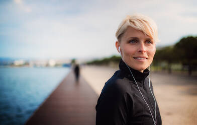 Porträt einer jungen Sportlerin mit Kopfhörern, die im Freien am Strand steht, Kopierraum. - HPIF20900