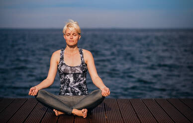 Front view portrait of young sportswoman doing yoga exercise on beach. Copy space. - HPIF20911