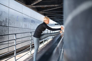 A portrait of young sportswoman with earphones doing exercise outdoors, stretching. - HPIF20914