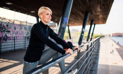 Eine junge Sportlerin mit Kopfhörern macht Übungen am Meer und dehnt sich. - HPIF20920