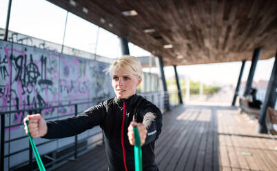 Eine junge Sportlerin mit elastischen Bändern, die im Freien in der Stadt trainiert. Raum kopieren. - HPIF20926