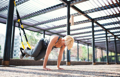 An attractive young sportswoman doing exercise with TRX fitness straps outdoors. - HPIF20932