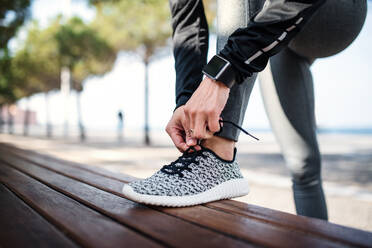 A midsection of young sportswoman with smartwatch outdoors in city, tying shoelaces. - HPIF20935