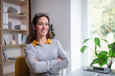 Attractive businesswoman sitting indoors in office, looking at camera. Copy space. - HPIF20972