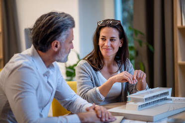 Mature architects sitting at the desk indoors in office, working. - HPIF20976