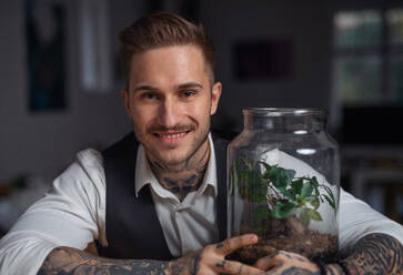 A businessman with plant terrarium sitting at the desk indoors in green office. - HPIF20992