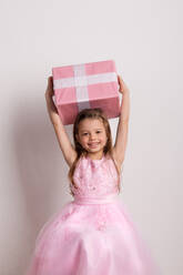Porträt eines kleinen Mädchens, das ein Geschenk oder eine verpackte Schachtel auf dem Kopf hält, Studioaufnahme auf weißem Hintergrund, Kopierraum. - HPIF21016
