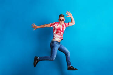 Ein junger Mann mit roter Sonnenbrille und gestreiftem T-Shirt springt in einem Studio. - HPIF21060