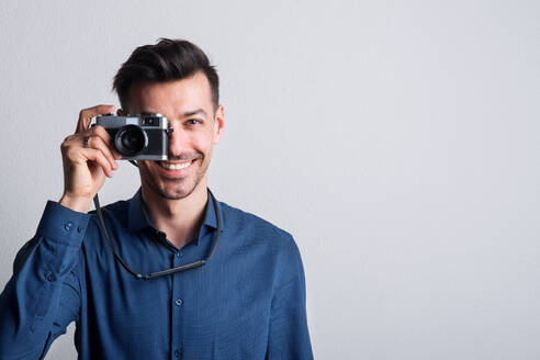 Porträt eines jungen, gut aussehenden Mannes in dunkelblauem Hemd in einem Studio mit einer Kamera vor dem Auge. Kopierraum. - HPIF21092