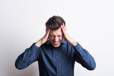 Porträt eines jungen Mannes mit starken Kopfschmerzen in einem Atelier, der sich den Kopf hält. - HPIF21095