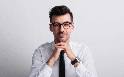 Porträt eines jungen Mannes mit Smartwatch und Brille in einem Studio, das Kinn auf die Hände gestützt. - HPIF21097