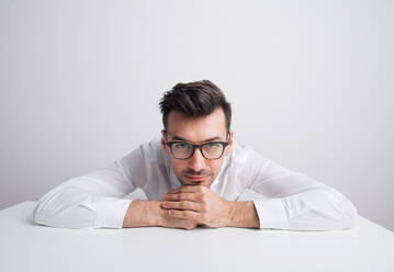Porträt eines jungen Mannes mit Brille und weißem Hemd in einem Studio auf weißem Hintergrund. - HPIF21099