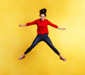 Young beautiful woman in a studio, jumping. Yellow background. Copy space. - HPIF21116