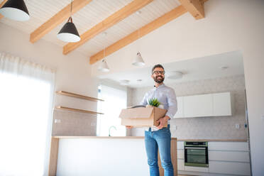 A mature man standing in unfurnished house, holding a box. A moving in new home concept. - HPIF21134