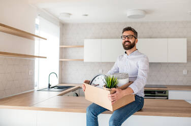 A mature man sitting in unfurnished house, holding a box. A moving in new home concept. - HPIF21137