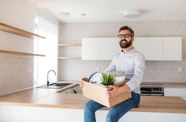 Ein reifer Mann, der in einem unmöblierten Haus sitzt und eine Kiste in der Hand hält - ein Konzept für den Einzug in ein neues Haus. - HPIF21137