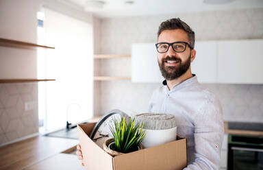 A mature man standing in unfurnished house, holding a box. A moving in new home concept. - HPIF21139