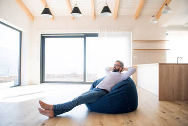 A happy mature man moving in new unfurnished house, sitting on bean bag. - HPIF21155