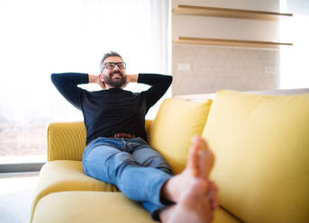 Cheerful mature man sitting on sofa in unfurnished house, moving in new home concept. - HPIF21169