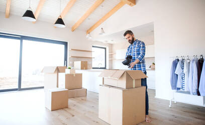 Ein reifer Mann mit Kisten, der in ein neues unmöbliertes Haus umzieht und auspackt. - HPIF21178