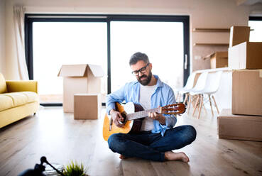 A mature man with boxes moving in new house, playing guitar. - HPIF21197