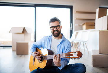 Ein reifer Mann mit Kisten zieht in ein neues Haus ein und spielt Gitarre. - HPIF21198