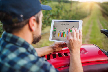 Ein reifer Landwirt mit einem Tablet, der neben einem Minitraktor in einer Obstplantage steht und die Erntemenge überprüft. - HPIF21220