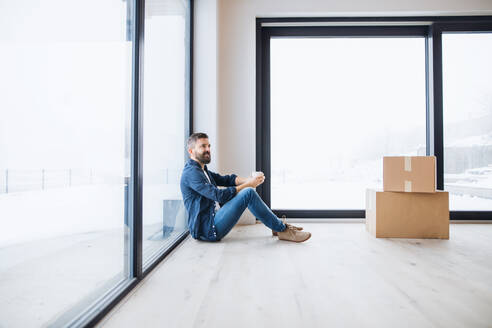 Ein reifer Mann mit Pappkartons auf dem Boden sitzend, der ein neues Haus einrichtet. Ein neues Hauskonzept. Raum kopieren. - HPIF21281