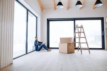 Ein reifer Mann mit Pappkartons auf dem Boden sitzend, der ein neues Haus einrichtet. Ein neues Hauskonzept. Raum kopieren. - HPIF21282