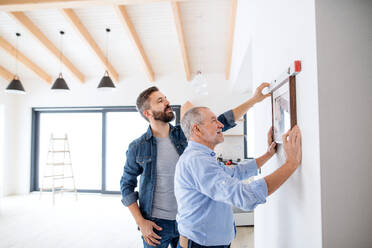 Ein älterer Mann hilft seinem Sohn beim Aufhängen von Bildern an der Wand, ein neues Wohnkonzept. - HPIF21313