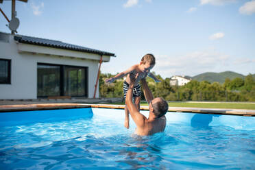 Ein Vater mit einem glücklichen kleinen Sohn, der im Schwimmbad im Freien spielt. - HPIF21327