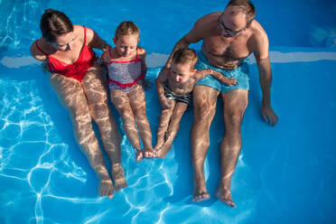 Junge Familie mit zwei kleinen Kindern sitzt im Schwimmbad im Freien, Blick von oben. - HPIF21328