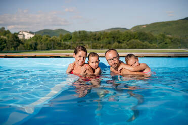 Junge Familie mit zwei kleinen Kindern im Schwimmbad im Freien, Blick in die Kamera. - HPIF21330