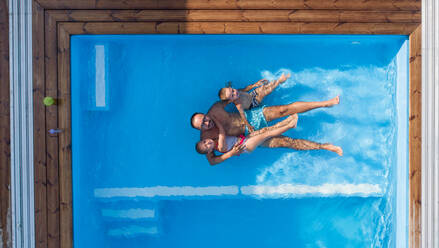 Top view of father with two small children sitting in swimming pool outdoors. - HPIF21333