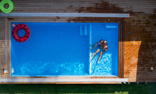 An aerial view of father with small children sitting in swimming pool outdoors. - HPIF21334