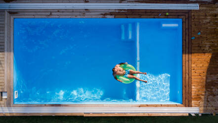 Luftaufnahme eines Mannes mit Sonnenbrille, der im Wasser eines Swimmingpools im Freien liegt. - HPIF21335