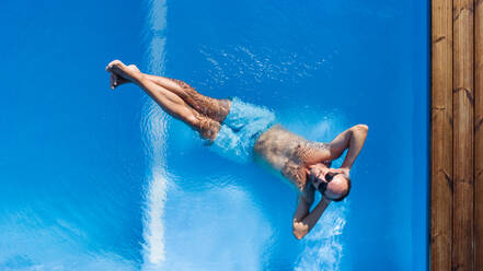 Draufsicht auf einen Mann mit Sonnenbrille, der in einem Schwimmbad im Freien im Wasser liegt. - HPIF21338