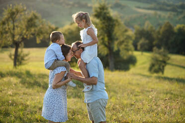 Happy young family with two small children standing on meadow outdoors at sunset. - HPIF21342