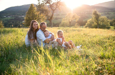 Happy young family with two small children sitting on meadow outdoors at sunset. - HPIF21354