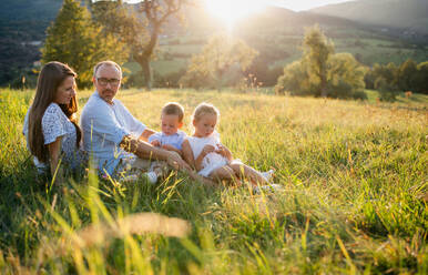 Glückliche junge Familie mit zwei kleinen Kindern sitzt bei Sonnenuntergang auf einer Wiese im Freien. - HPIF21355