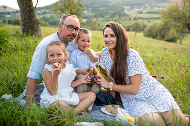 Eine junge Familie mit zwei kleinen Kindern auf einer Wiese im Freien beim Picknick. - HPIF21360