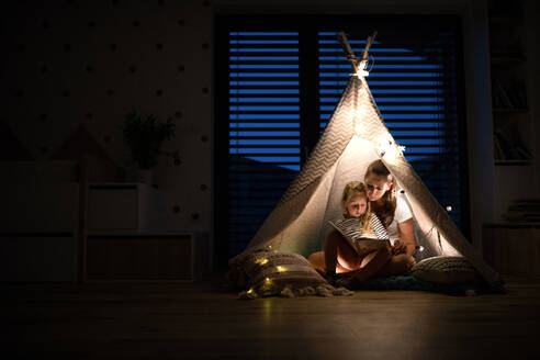 Junge Mutter mit kleiner Tochter sitzt im Schlafzimmer und liest ein Buch. - HPIF21364