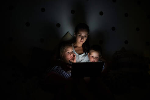 Junge Mutter mit Kindern, die abends im Schlafzimmer sitzen und einen Laptop benutzen. - HPIF21367