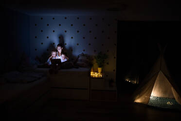 Young mother with children sitting indoors in bedroom in the evening, using laptop. - HPIF21368