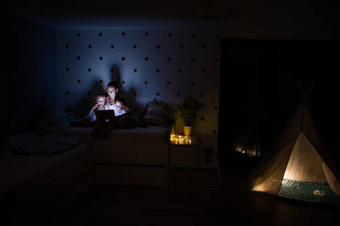 Junge Mutter mit Kindern, die abends im Schlafzimmer sitzen und einen Laptop benutzen. - HPIF21368
