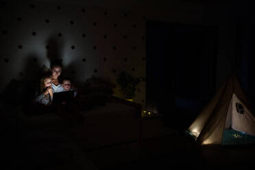 Young mother with children sitting indoors in bedroom in the evening, using laptop. - HPIF21369