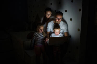 Front view of family with children sitting indoors in bedroom, using laptop. - HPIF21373