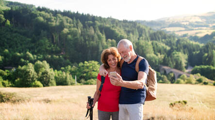 A senior tourist couple hikers standing in nature, taking selfie. - HPIF21398