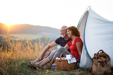 Ein älteres Touristenpaar mit Picknickkorb sitzt bei Sonnenuntergang in der Natur und ruht sich aus. - HPIF21425