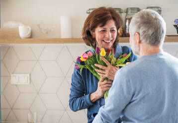 Ein verliebtes älteres Paar in einem Haus, der Mann schenkt der glücklichen Frau Blumen. - HPIF21442
